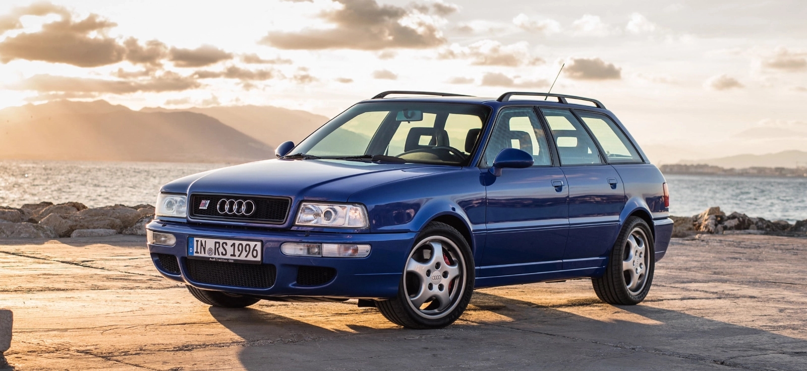 Plavi Audi RS2 Avant karavan parkiran na obali pored mora tokom zalaska sunca