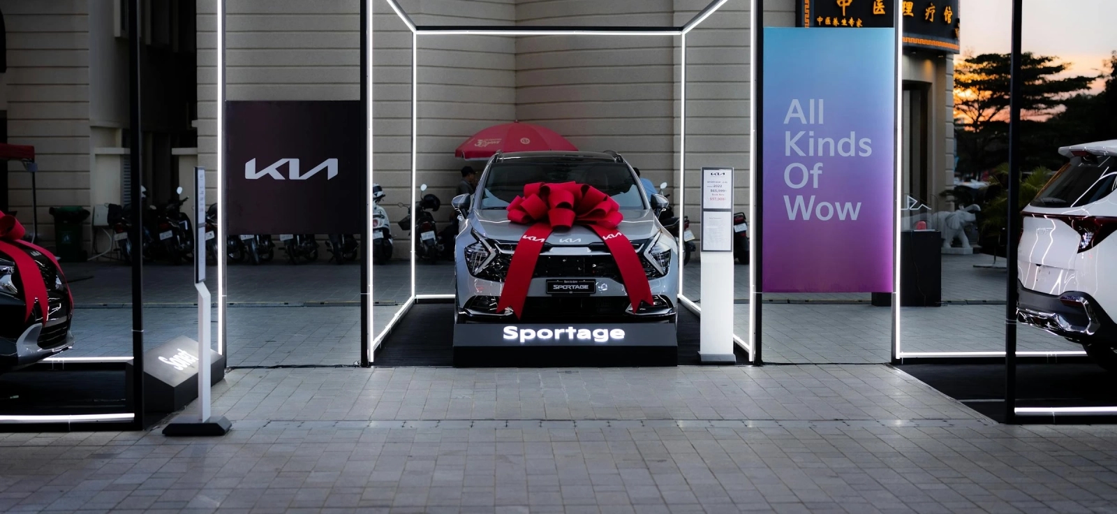 Automobil marke Kia parkiran u salonu, sa crvenom mašnom preko haube spreman za prodaju.