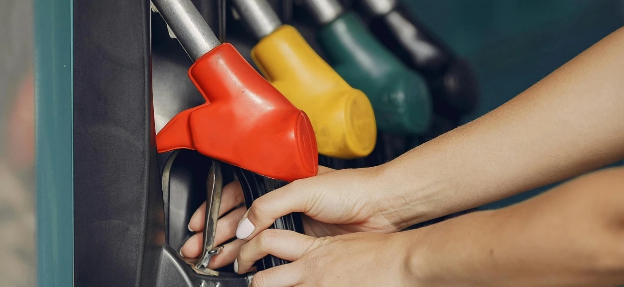 Ruka vozača bira pištolj za točenje goriva na pumpi, prikaz razlike između premium i standardnog goriva i aditiva u gorivu