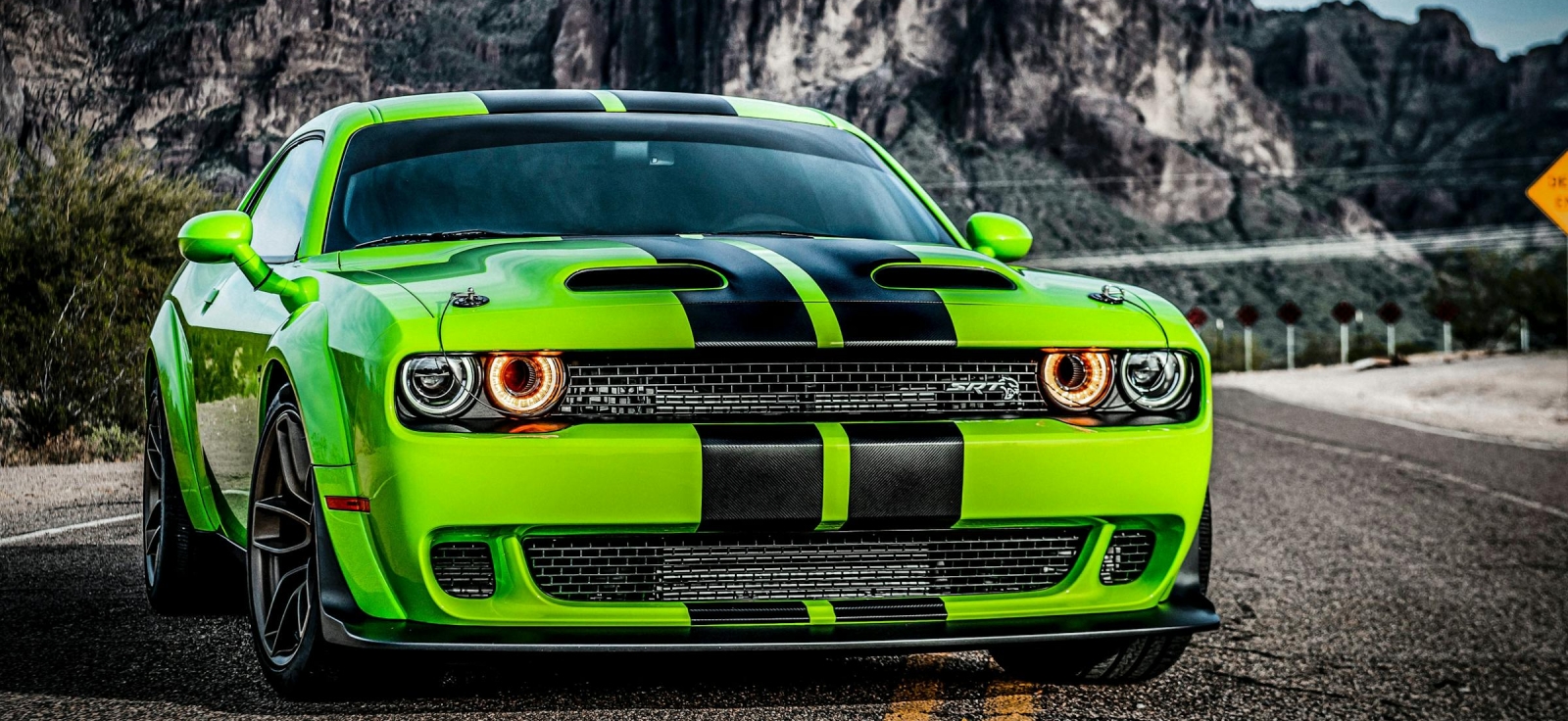 Prednji profil zelenog Dodge Challenger SRT Hellcat-a sa crnim prugama na asfaltu – ikona moderne muscle kulture sa 707 konjskih snaga
