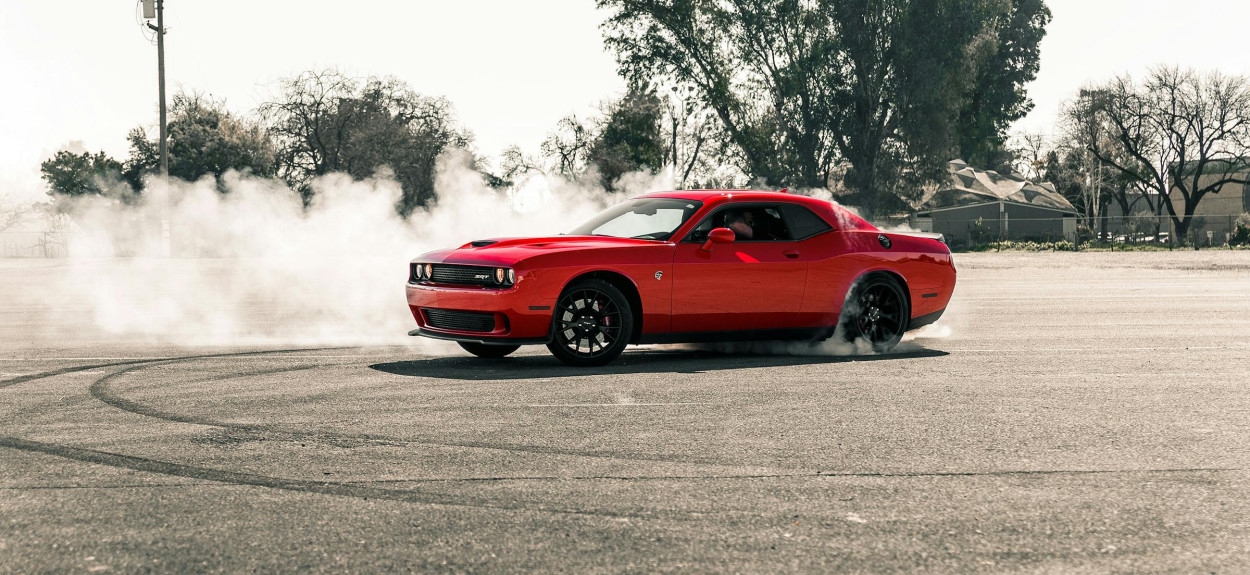 Crveni Dodge Challenger Hellcat u agresivnom driftu, dok guma nestaje u dimu, demonstrirajući sirovi obrtni moment V8 HEMI motora