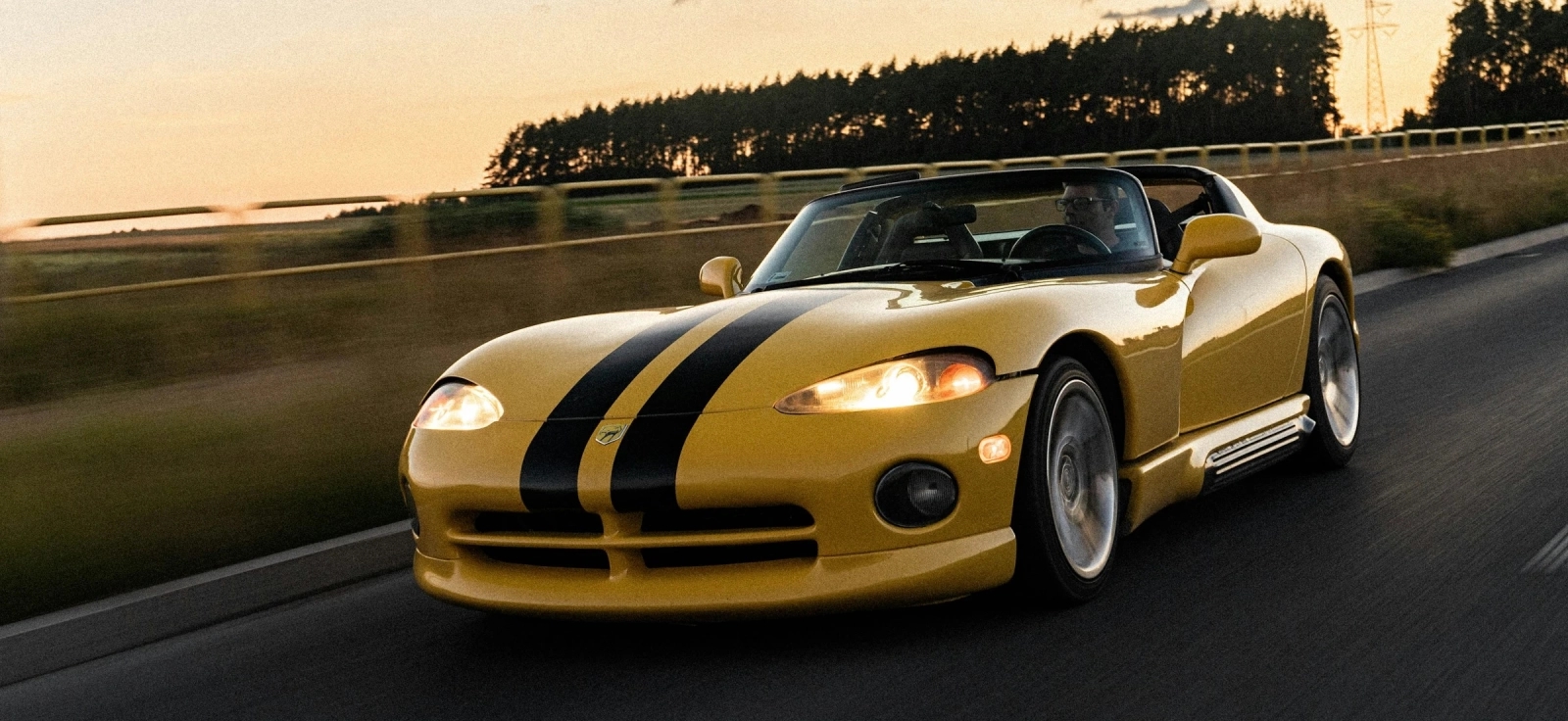 Žuti Dodge Viper RT/10 prve generacije sa prepoznatljivim crnim trkačkim trakama u vožnji tokom zalaska sunca