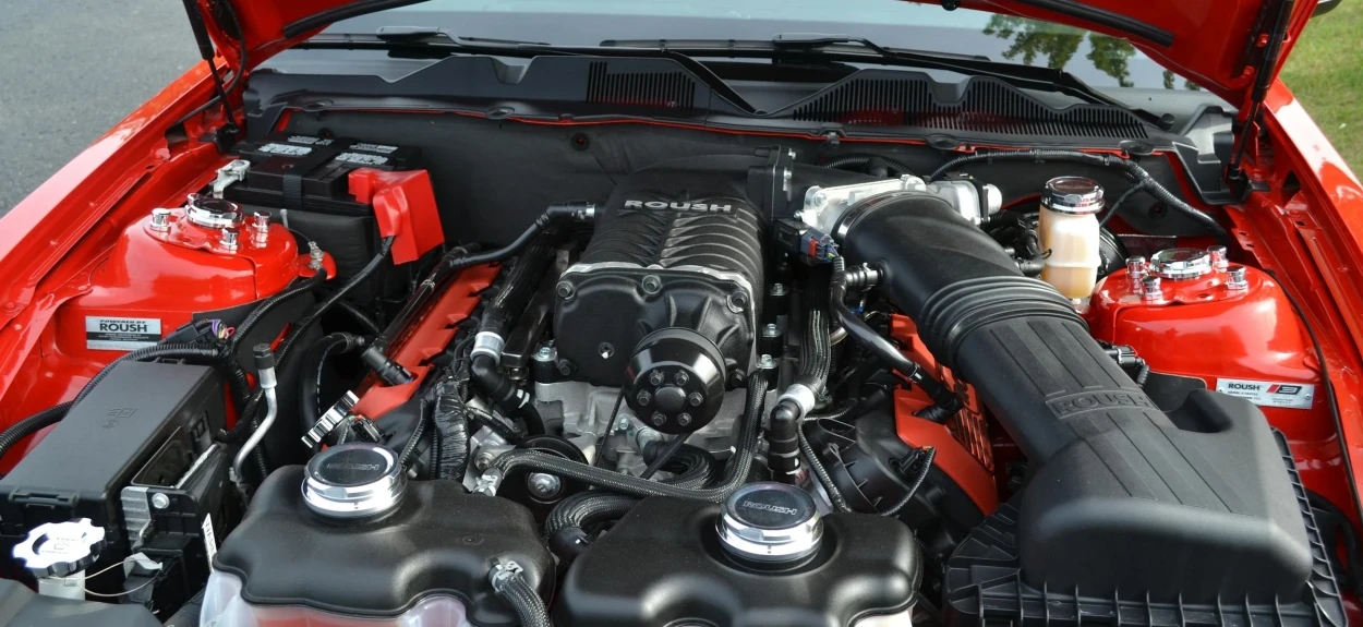 Crveni automobil sa otvorenom haubom gde se vidi motor.