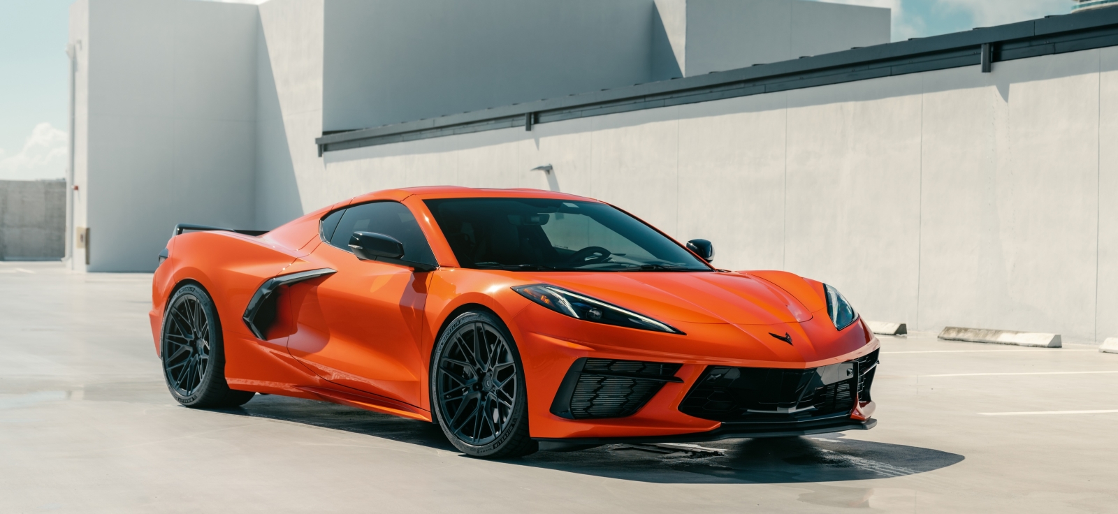 Narandžasta Chevrolet Corvette C8 sa središnjim motorom na parkingu, savremeni američki superautomobil koji ubrzava do stotke ispod 3 sekunde