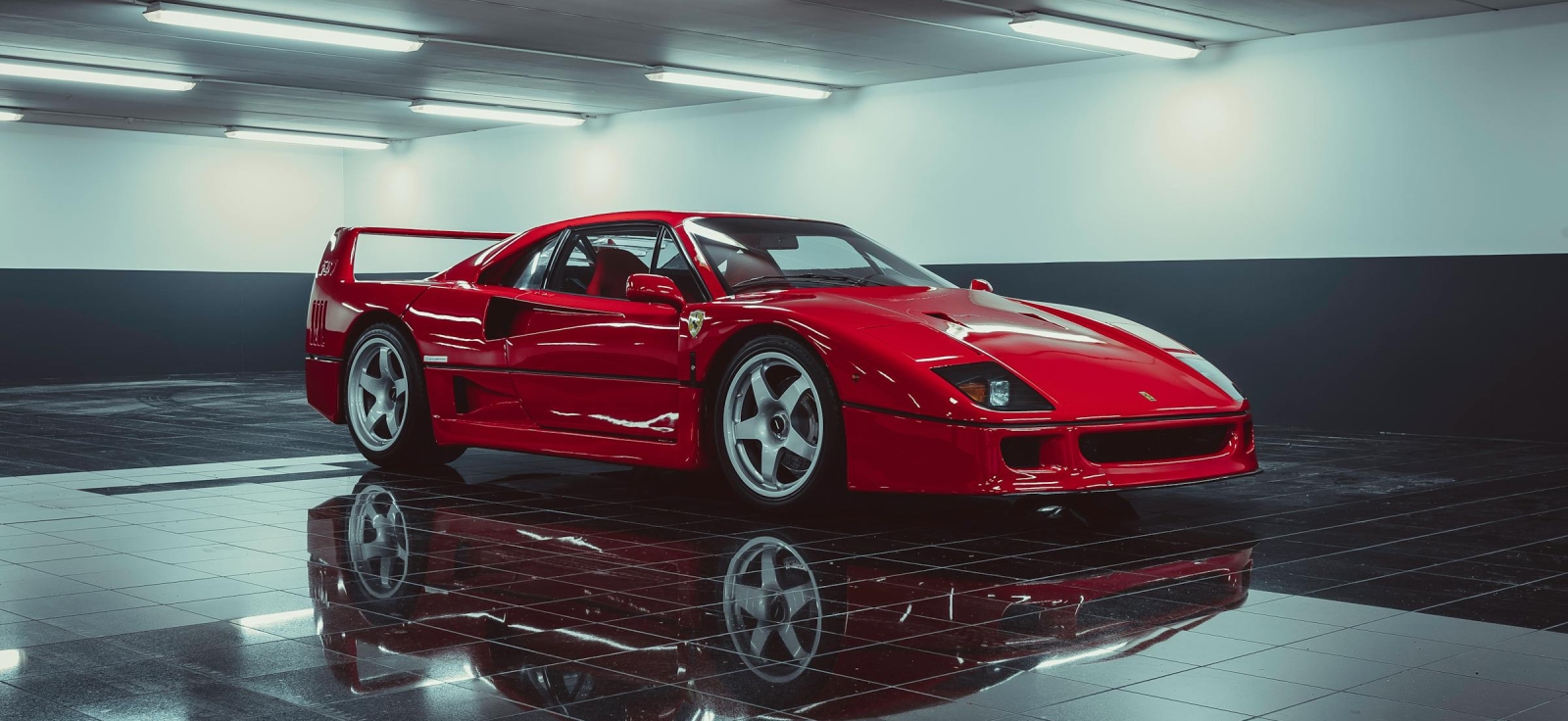 Crveni Ferrari F40 parkiran u modernoj studijskoj garaži sa visokim sjajem poda, prikazuje bezvremenski dizajn poslednjeg Enzovog superautomobila