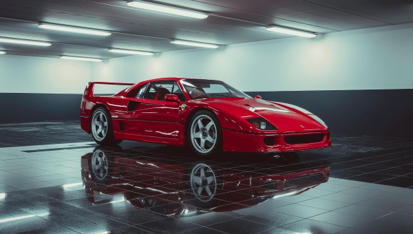 Crveni Ferrari F40 parkiran u modernoj studijskoj garaži sa visokim sjajem poda, prikazuje bezvremenski dizajn poslednjeg Enzovog superautomobila