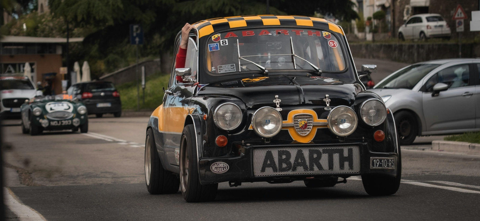 Klasični crno žuti trkački Fiat Abarth sa otvorenim poklopcem motora i upaljenim svetlima na asfaltnoj stazi