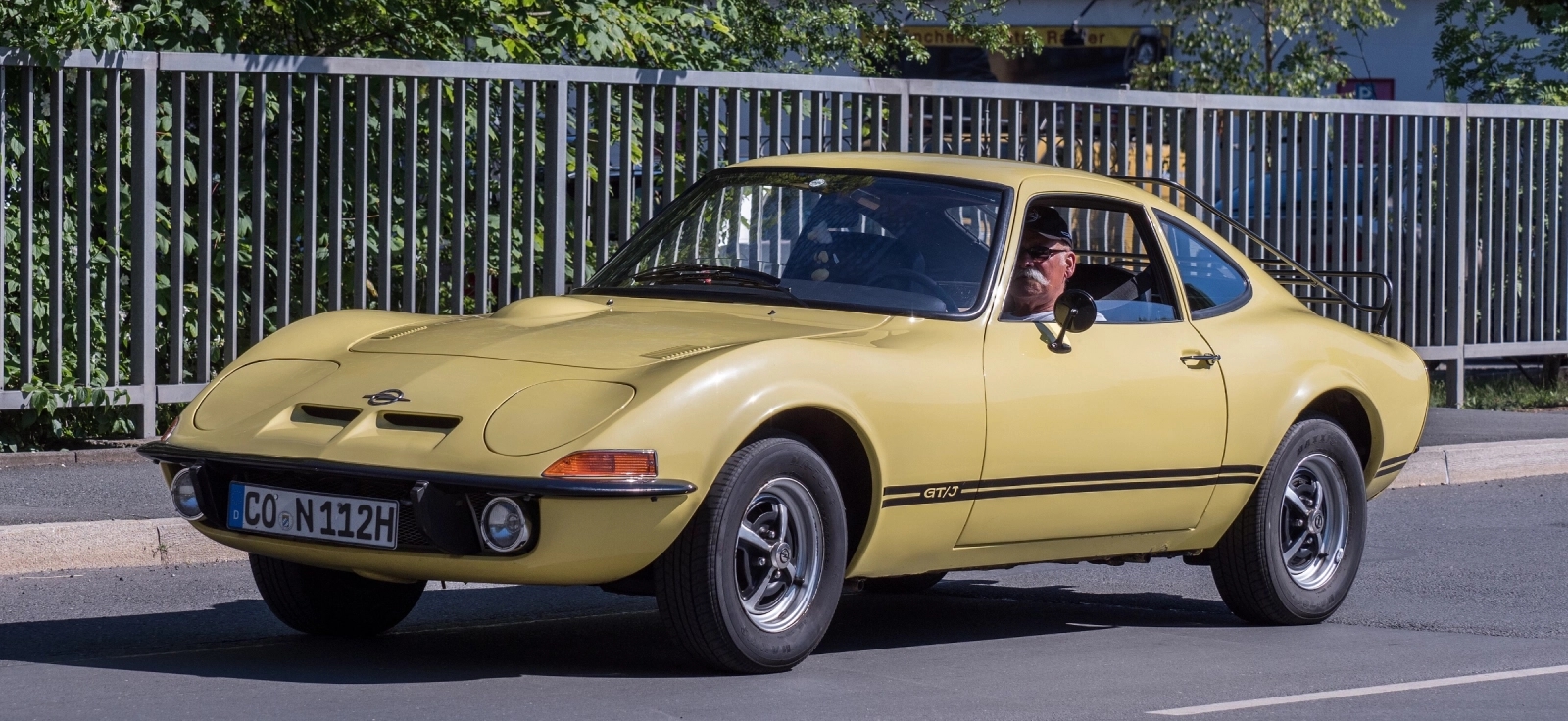 Zuti sportski kupe Opel GT poznat kao nemacka korveta u voznji na drumu pored zastitne ograde