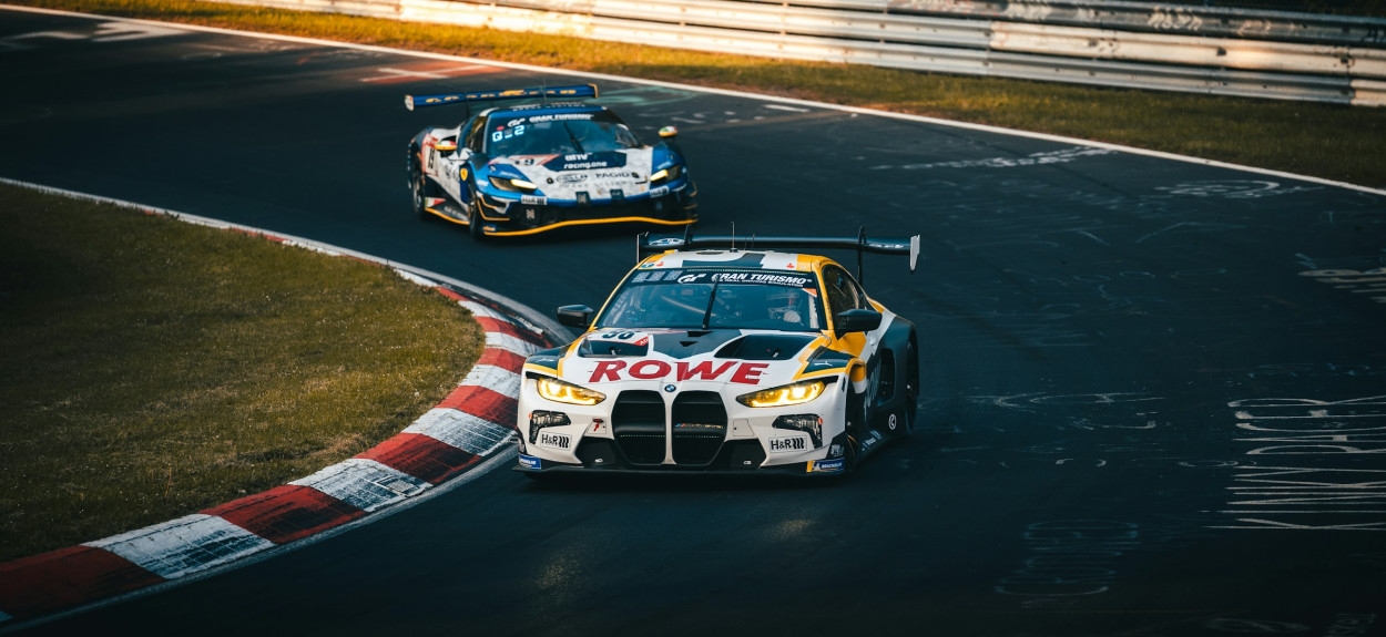 Trkački BMW M4 GT3 Rowe Racing tima savladava krivinu na Nürburgringu pod dnevnim svetlom.