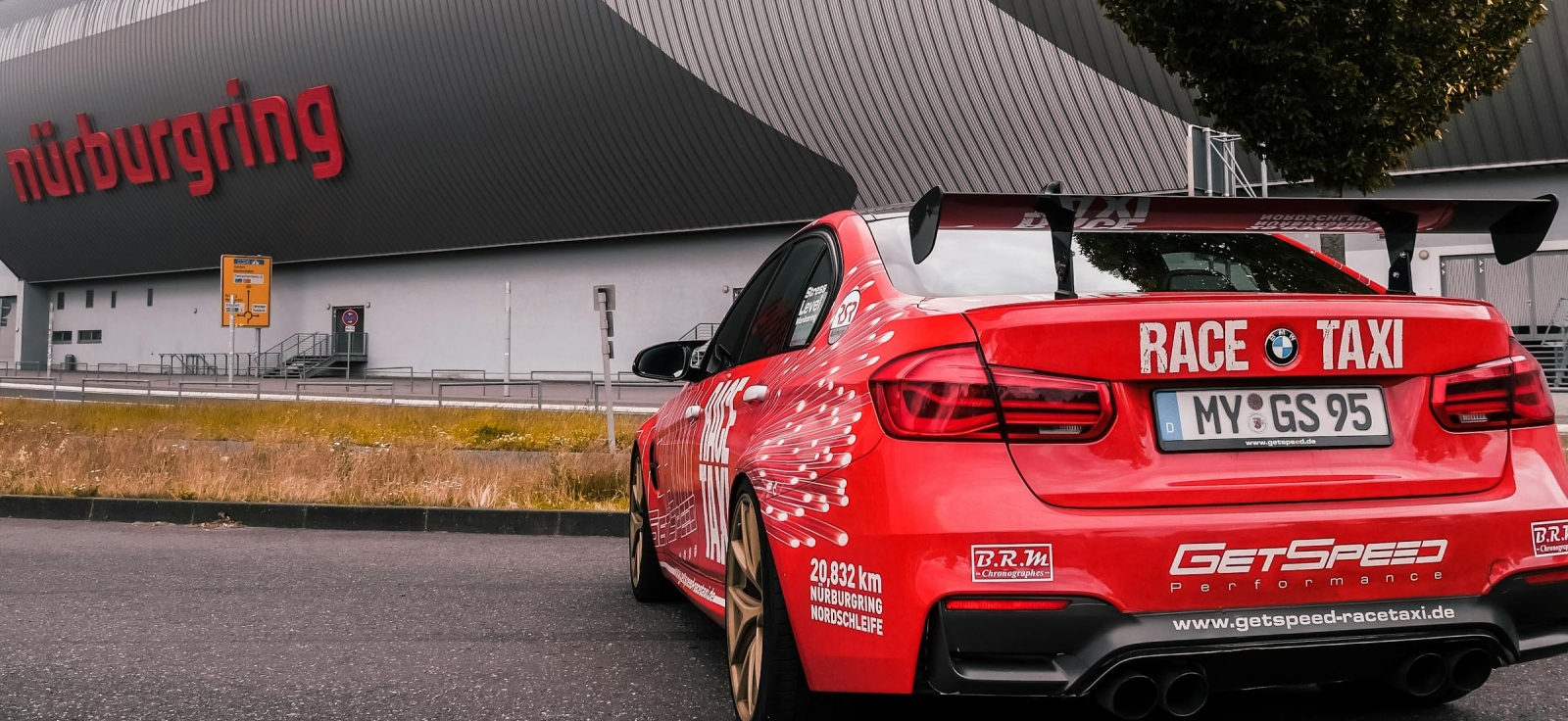 Crveni BMW M4 Race Taxi parkiran ispred glavnog Nürburgring objekta spreman za turističku vožnju.