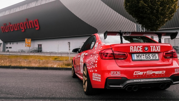 Crveni BMW M4 Race Taxi parkiran ispred glavnog Nürburgring objekta spreman za turističku vožnju.