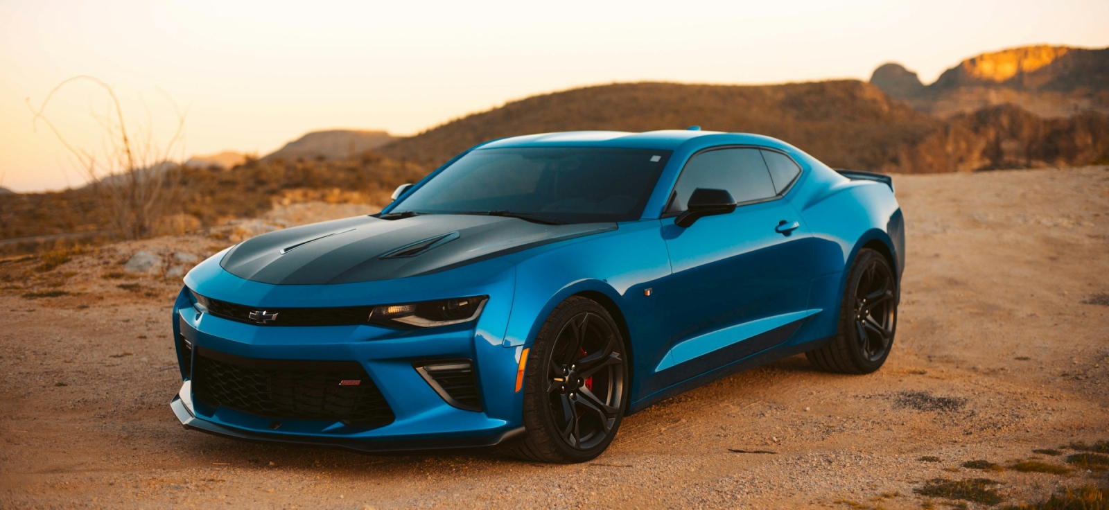 Moderni plavi Chevrolet Camaro šeste generacije snimljen u pustinjskom okruženju tokom zalaska sunca.