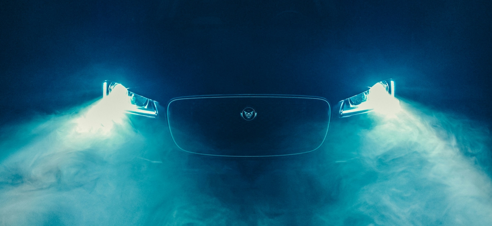 Prednji deo modernog Jaguar automobila sa upaljenim LED svetlima u plavom dimu i magli
