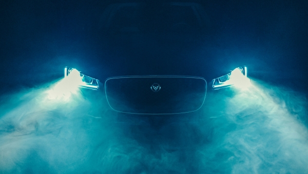 Prednji deo modernog Jaguar automobila sa upaljenim LED svetlima u plavom dimu i magli