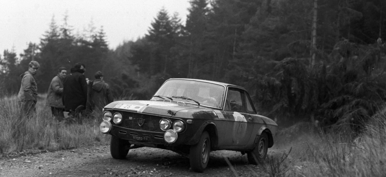 Istorijski crno-beli snimak starog reli automobila na blatnjavoj šumskoj stazi iz ranog perioda relija