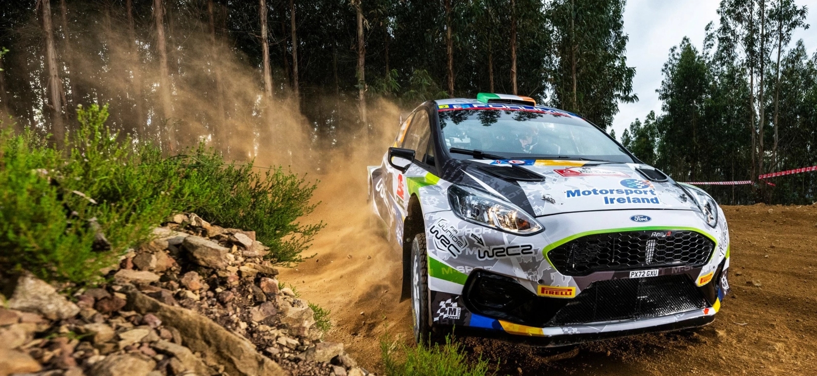 Savremeni reli automobil u brzoj vožnji kroz šumski put, podiže prašinu u zavoju