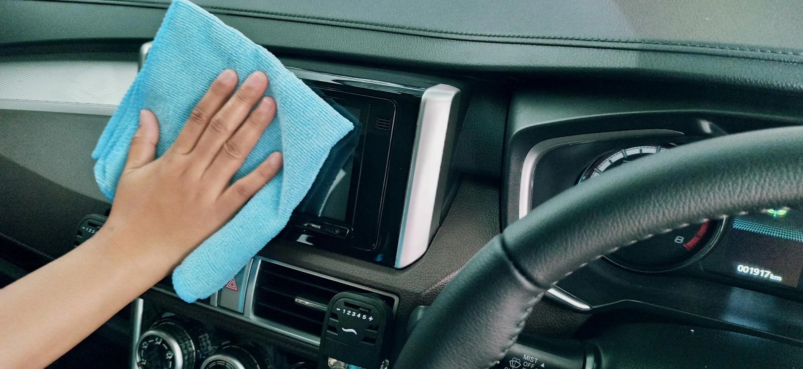 Čovek koji briše unutrašnjost svog automobila plavom krpom.