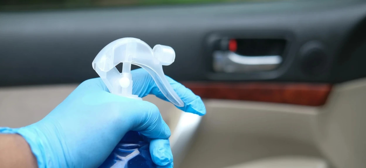 Ruka koja drži plavu tečnost za pranje enterijera vozila u boci sa pumpicom.