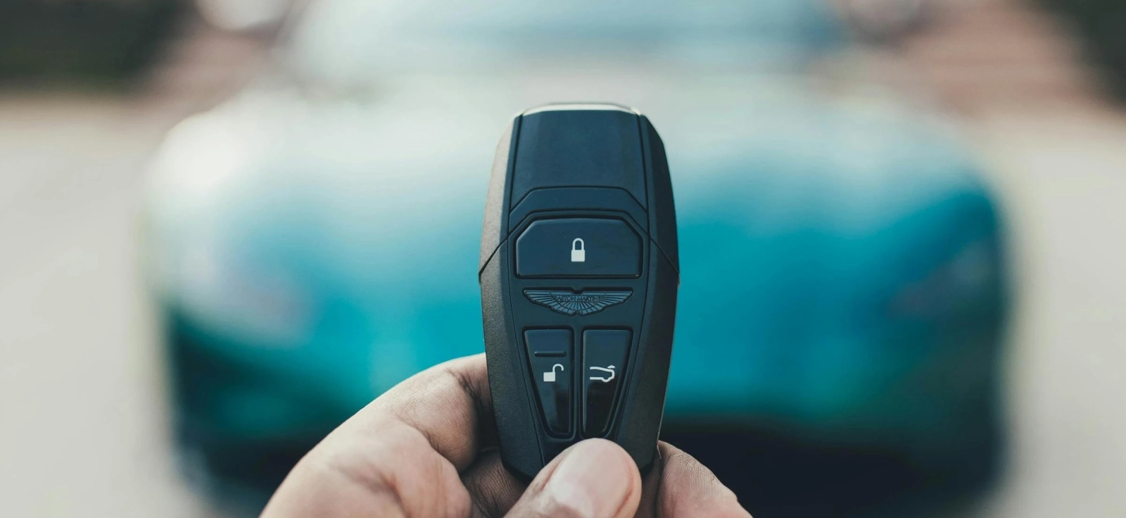 Čovek koji drži ključ od automobila sa zelenim automobilom u pozadini.