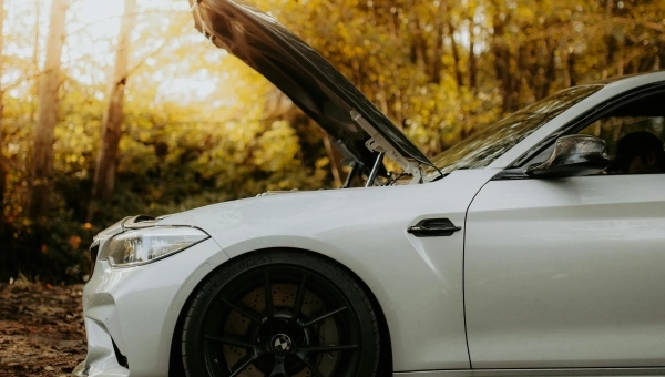 Beli auto sa otvorenom haubom pored puta u sumi, jesenji prizor.