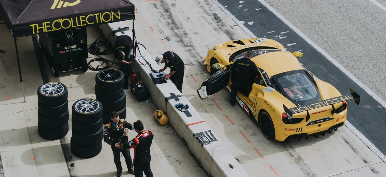 Mehaničari menjaju gume na žutom GT trkačkom automobilu tokom pit-stopa na stazi, prikaz rada tima u motosportu