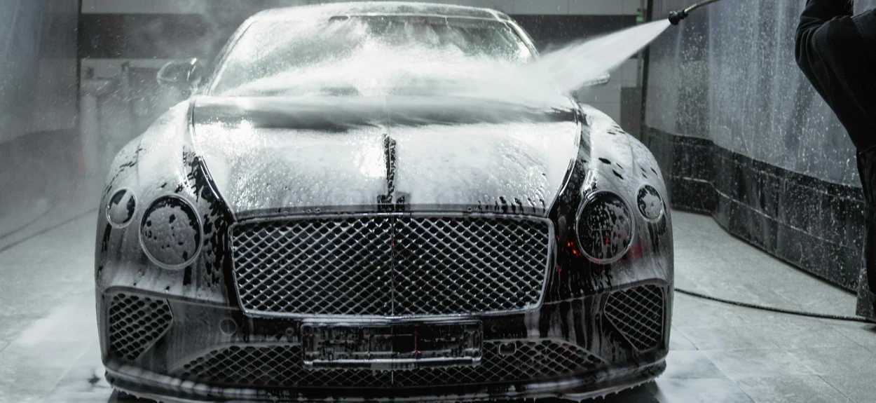 Crni auto sa penom na sebi u salonu za pranje automobila.