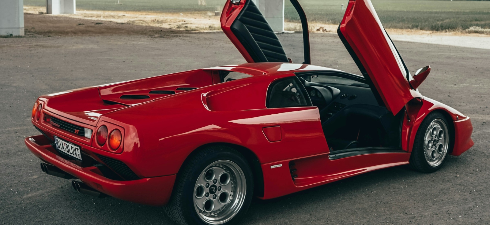 Crveni Lamborghini Diablo sa otvorenim makaze vratima ispod mosta
