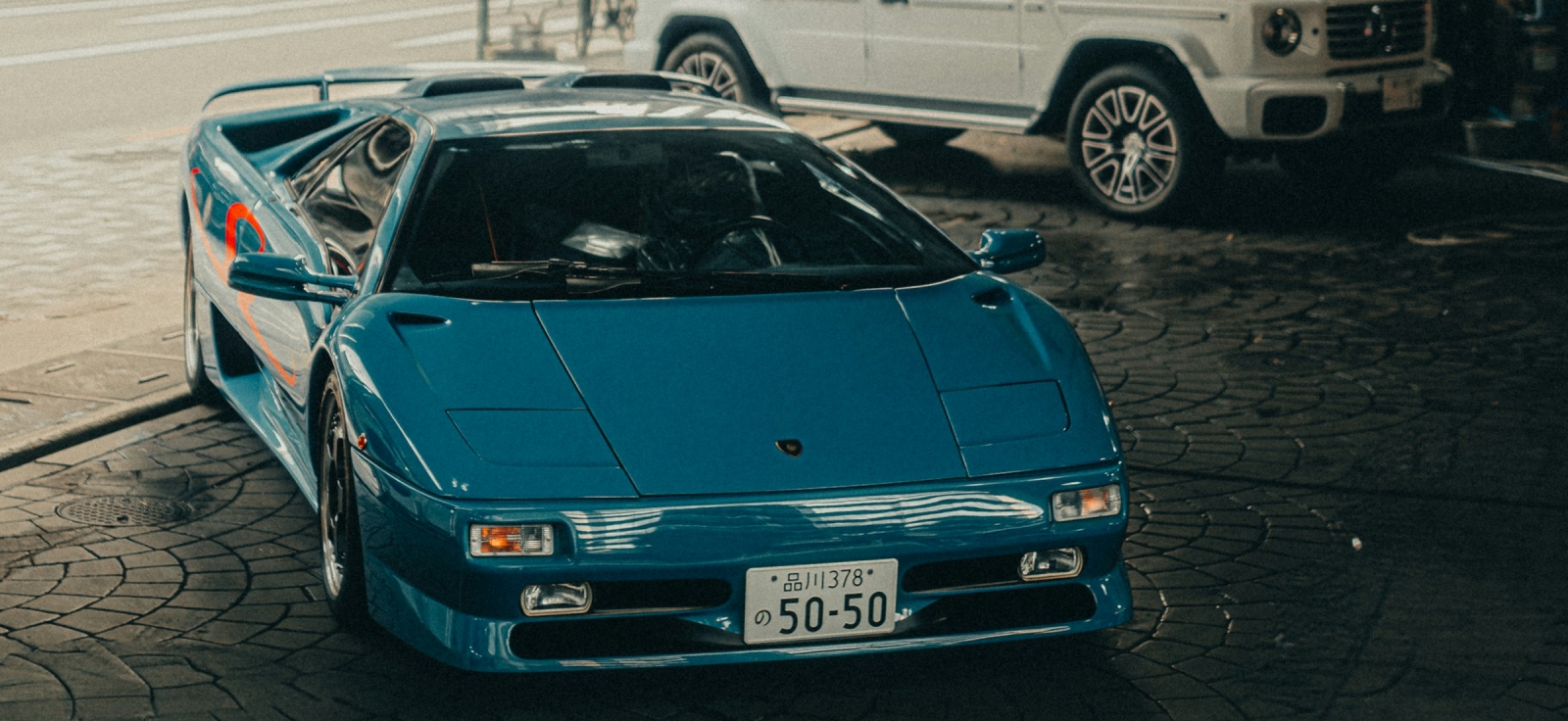 Plavi Lamborghini Diablo parkiran na kockastoj kaldrmi pored belog terenca