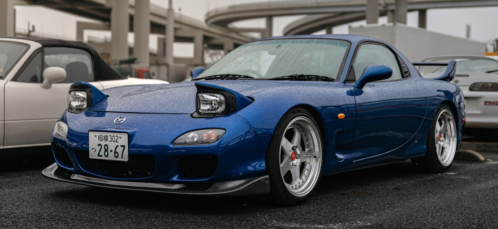 Prednji deo plave Mazde RX-7 FD sa otvorenim pop-up svetlima parkirane na skupu u Japanu