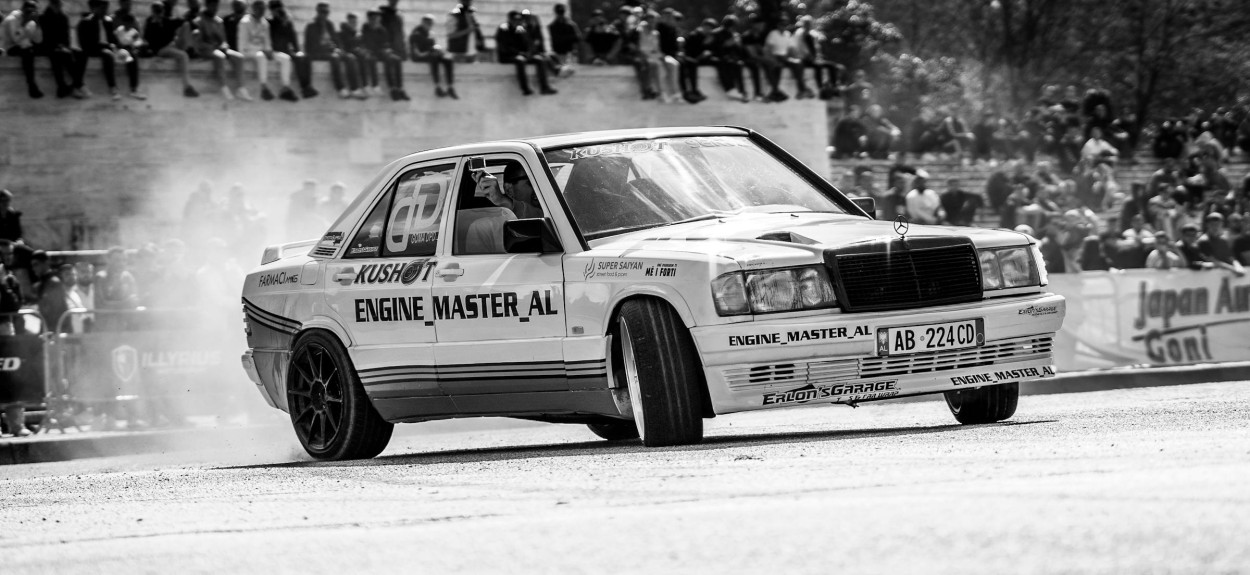 Crno-bela fotografija modifikovanog Mercedes 190E Cosworth u trkačkoj akciji na stazi sa natpisom Engine Master na vratima