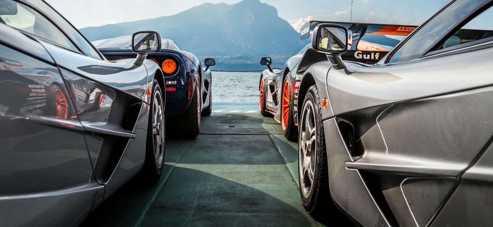 Luksuzni automobili parkirani na ivici mora sa pogledom na planinu.