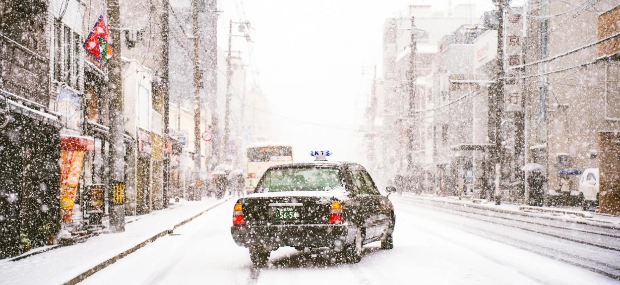 Crni automobil na snegu na sred ulice dok sneg veje.
