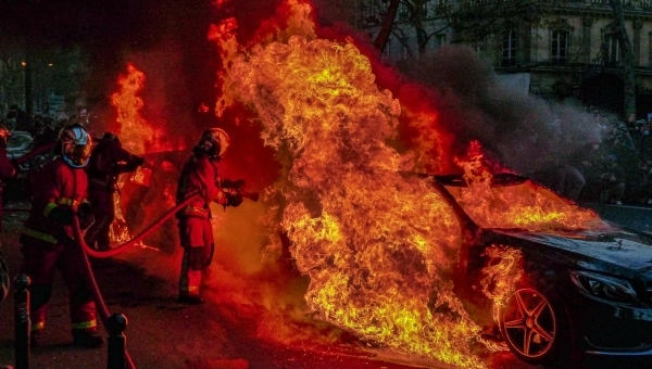 Auto koji gori i vatrogasni tim koji gasi požar.