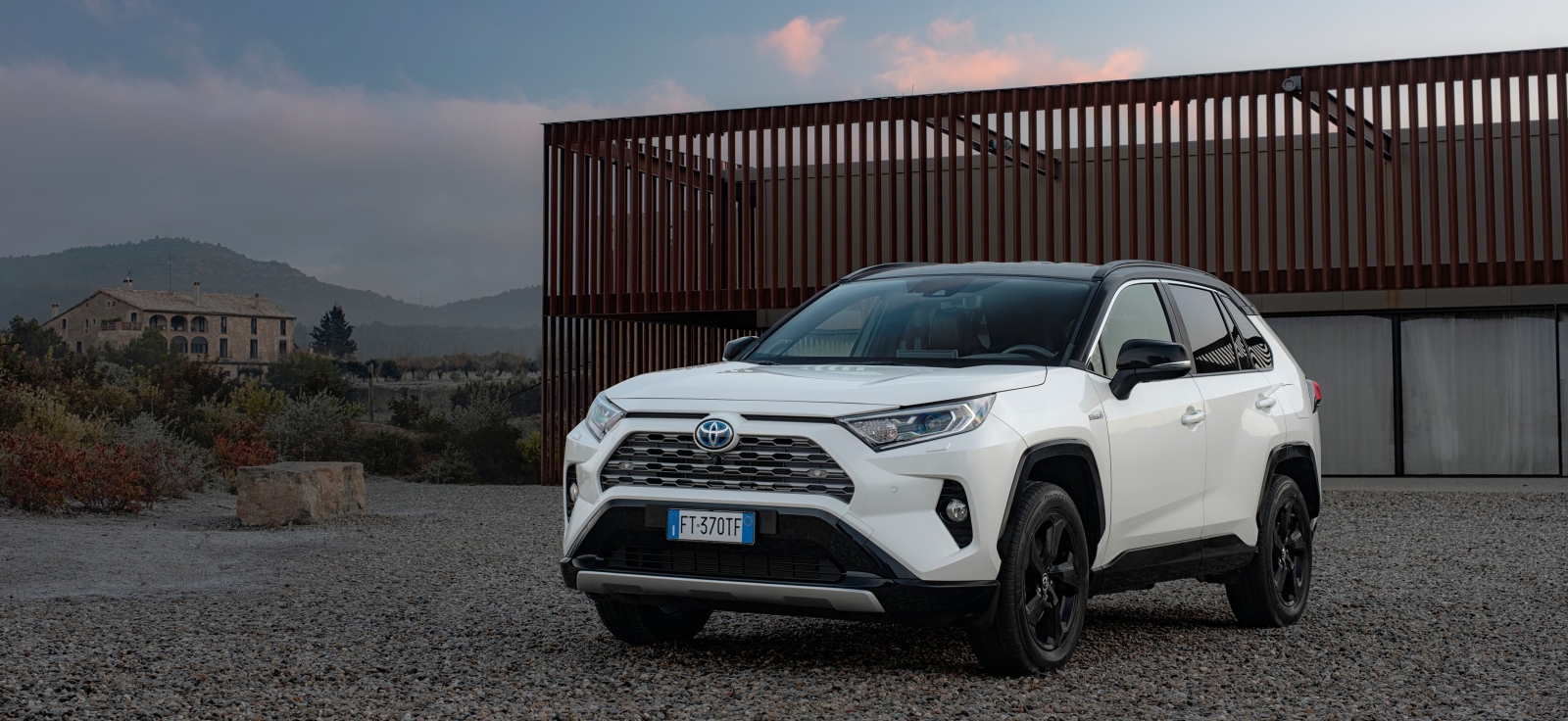 Bela Toyota RAV4 hibrid pete generacije parkirana ispred modernog objekta – najpouzdaniji polovni SUV model na tržištu