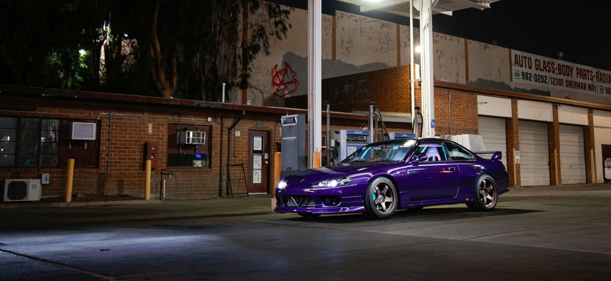 Ljubičasta Nissan Silvia S15 parkirana ispod osvetljenja na benzinskoj stanici noću, prikazujući agresivan prednji branik i spuštenu siluetu