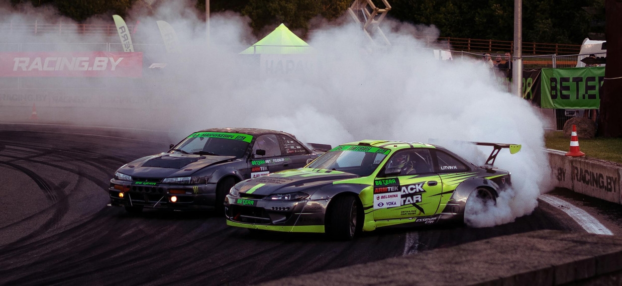 Dva modifikovana Nissan Silvia S15 automobila u tandemskom driftu na stazi sa velikim oblakom dima iz zadnjih guma