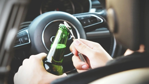 Čovek koji otvara pivo ispred volana dok vozi auto.