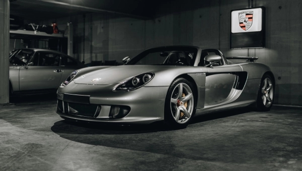 Porsche Carrera GT parkiran u garaži sa fokusom na prednji deo i prepoznatljiva prednja svetla ispod Porsche amblema na zidu