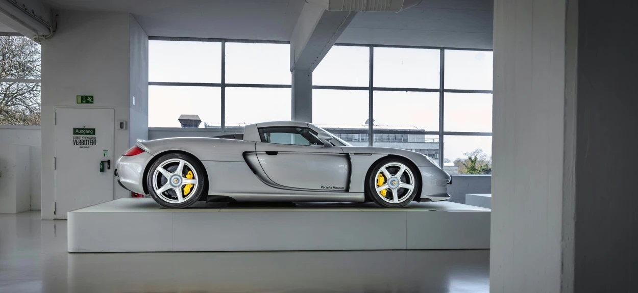 Srebrni Porsche Carrera GT prikazan iz profila na belom izložbenom postolju u salonu