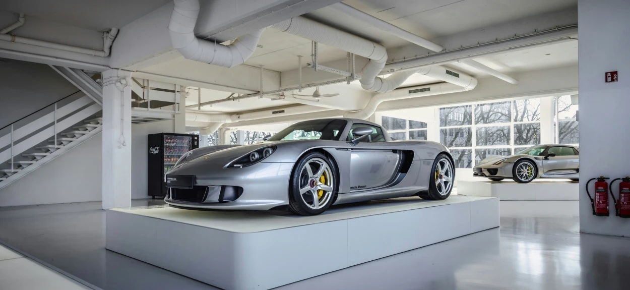 Prednji desni ugao Porsche Carrera GT superautomobila u svetlom fabričkom okruženju sa vidljivim žutim kočionim čeljustima