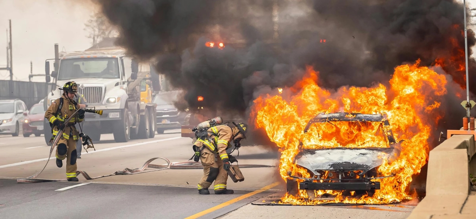 Vatrogasci gase zapaljeni automobil na autoputu tokom letnjeg dana uz gust dim i vatru