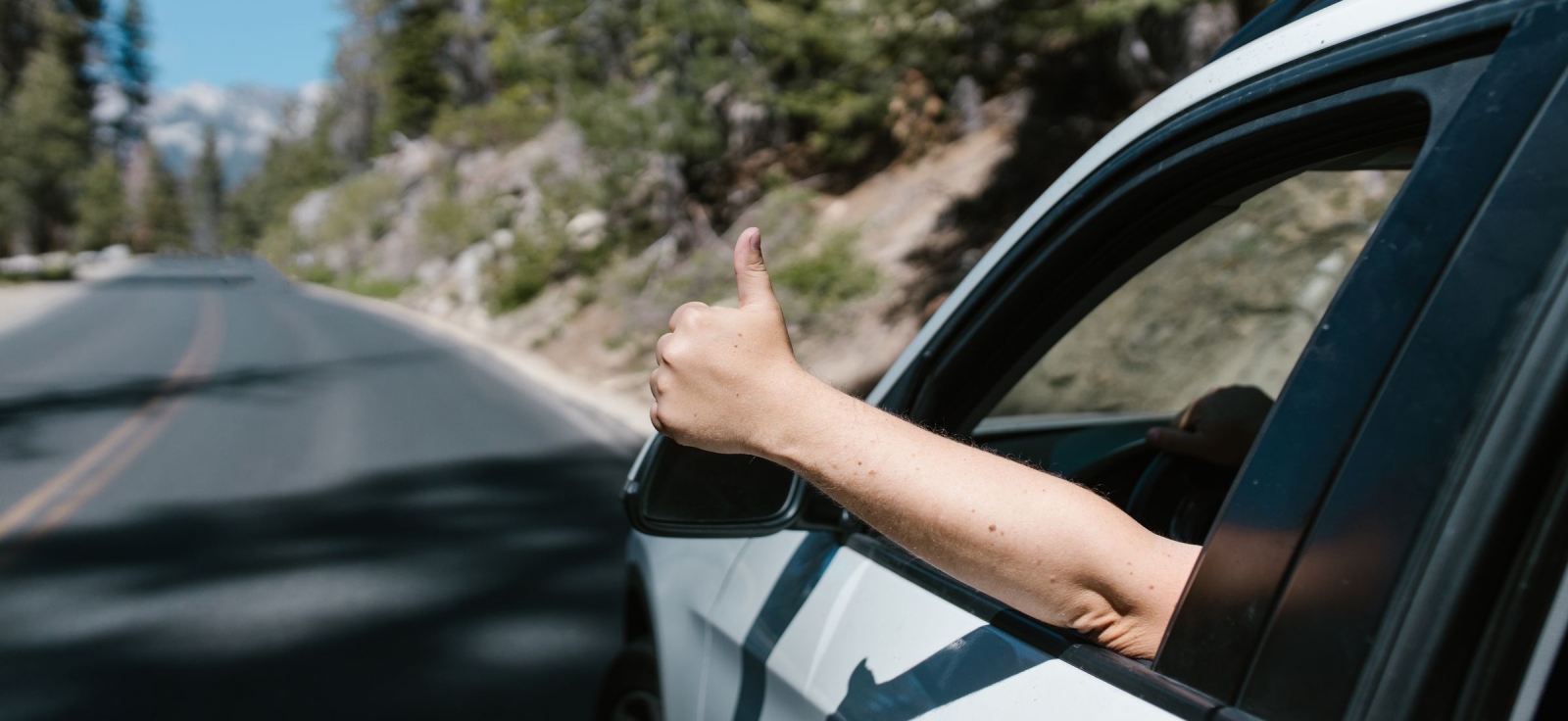 Vozač pokazuje palac na gore kroz prozor automobila tokom sigurne vožnje ka moru