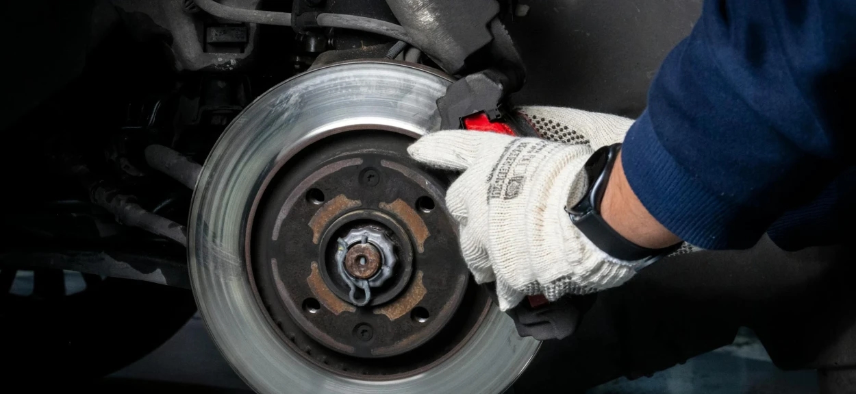 Mehaničar menja kočione pločice i disk na automobilu tokom redovnog servisa