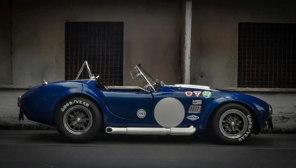 Bočna silueta plave Shelby Cobra 427 parkirane ispred industrijskog zida, klasični američki roadster sa britanskom šasijom