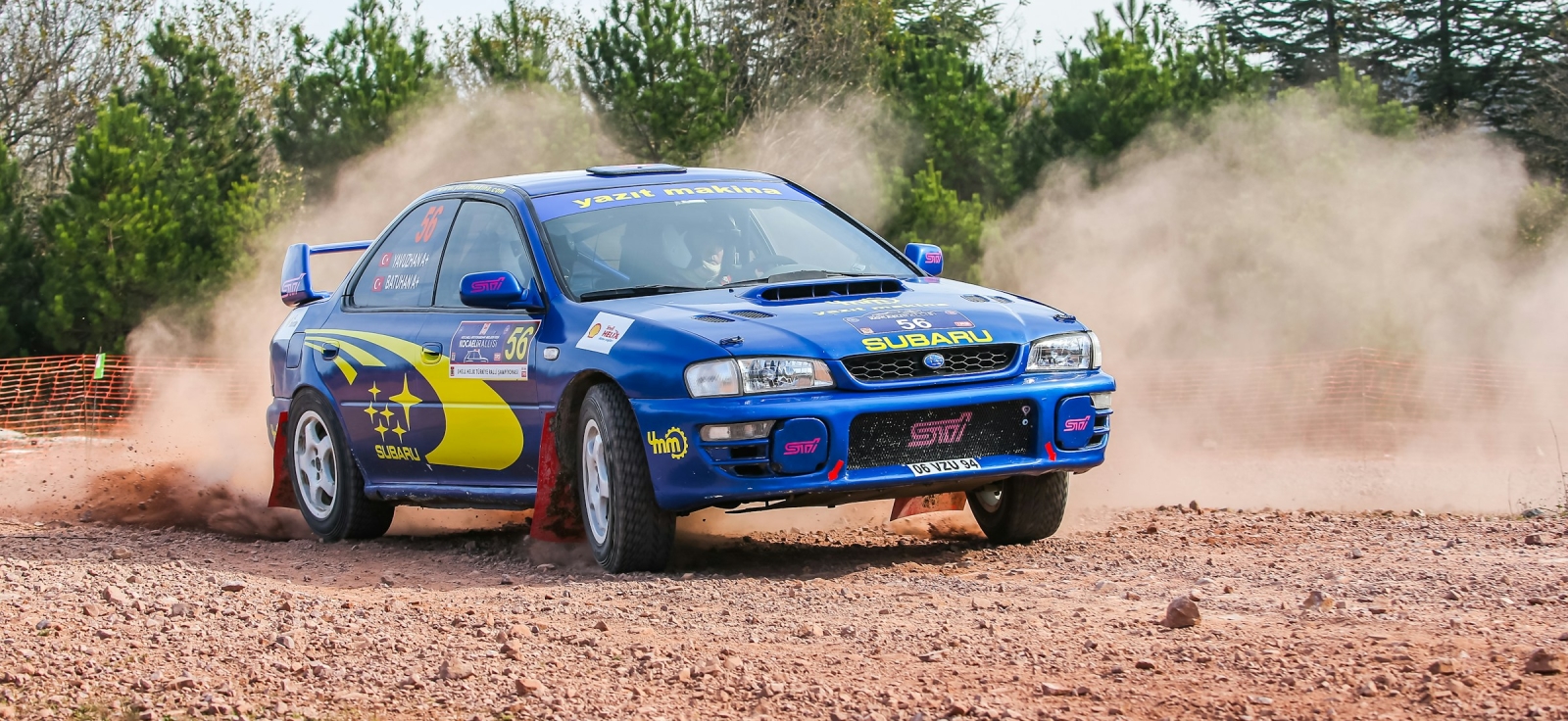 Plavi Subaru Impreza WRX STI u punoj brzini na reli stazi dok podiže prašinu, prikazujući moć simetričnog pogona na sva četiri točka.