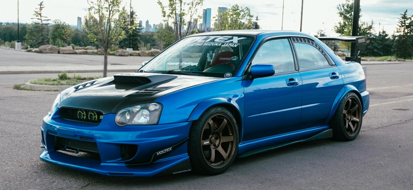 Modifikovani plavi Subaru WRX STI "Blob-eye" sa zlatnim felnama i spuštenim sportskim vešanjem, simbol moderne JDM tuning kulture.