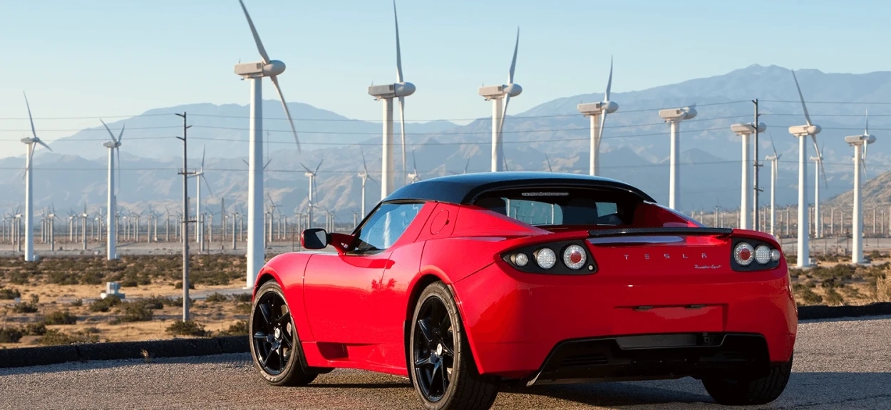 Tesla Roadster 2008 crveni električni automobil parkiran ispred vetroturbina u pustinji