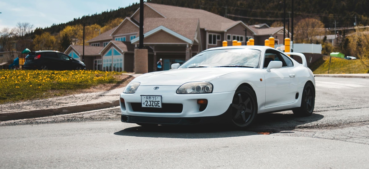 Koseg bočnog pogleda na belu Toyota Supra MK4, čisti fabrički izgled, parkirana na asfaltu ispred zgrade