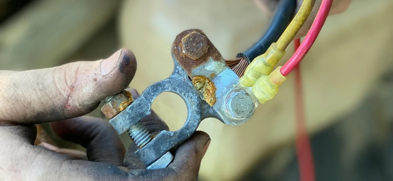 Čovek drži kleme akumulatora i proverava kontakte na automobilu – oksidacija i problemi sa strujom u autu