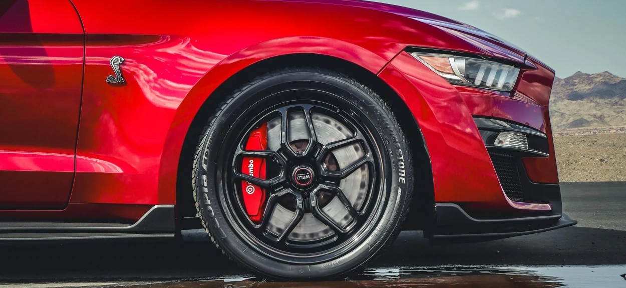 Crveni automobil sa fokusom na niskoprofilne gume sa refleksijom na vodu.